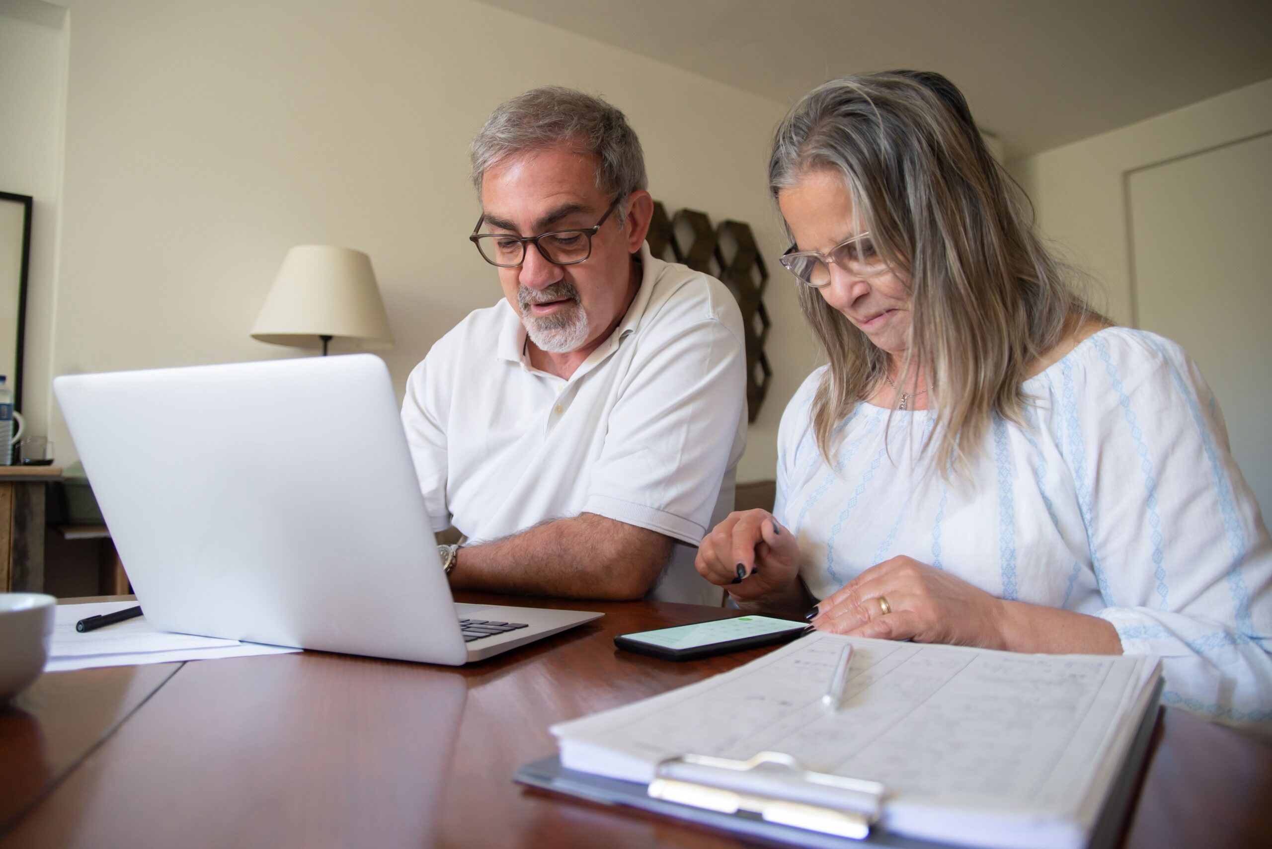 Senior couple working together on documents with laptop and phone at home